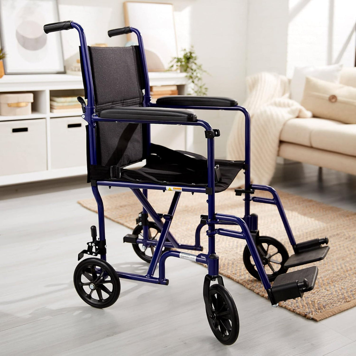The McKesson Lightweight Aluminum Transport Chair, featuring blue framing and black armrests, seat, and footrests, is placed in a bright living room with modern light-colored decor for a practical mobility solution.