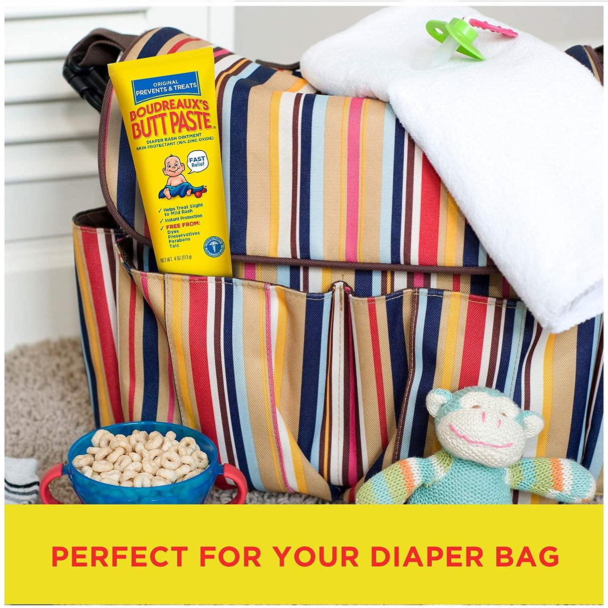 A striped diaper bag sits on a surface next to Boudreauxs Butt Paste Rash Cream (Original), a white towel, cereal bowl, and green-white stuffed monkey; bottom text reads “PERFECT FOR YOUR DIAPER BAG.”.