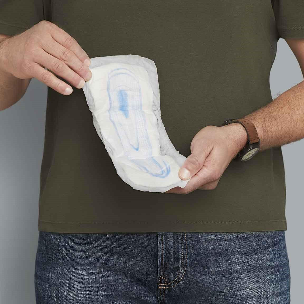 A person in a green shirt and jeans holds Depend Incontinence Guards for Men by Depend with both hands, displaying the product in front of their torso.