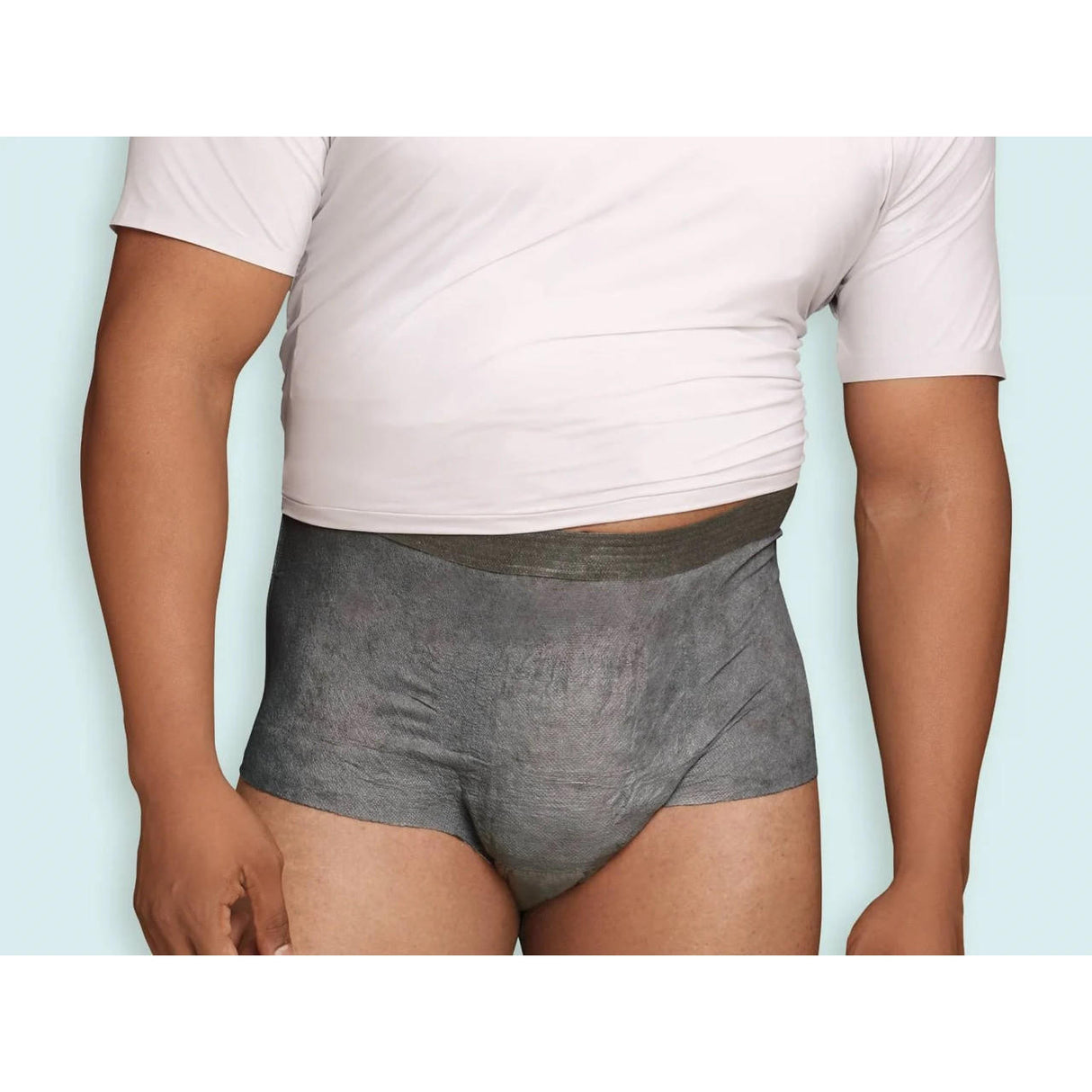 A person wearing a white t-shirt and gray Depend Mens Real Fit Absorbent Underwear, Maximum, stands against a light blue background with the t-shirt slightly lifted to show the Depend waistband.