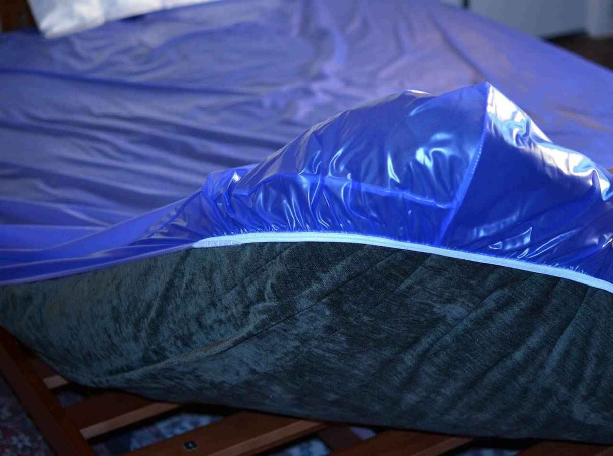 A close-up of a bed with the Gary Heavy Duty Plastic Mattress Cover Protector, Twin by Gary, partially unzipped to reveal a dark gray mattress. The wooden bedframe and blue bedding are visible, and the cover offers medical-grade vinyl protection.