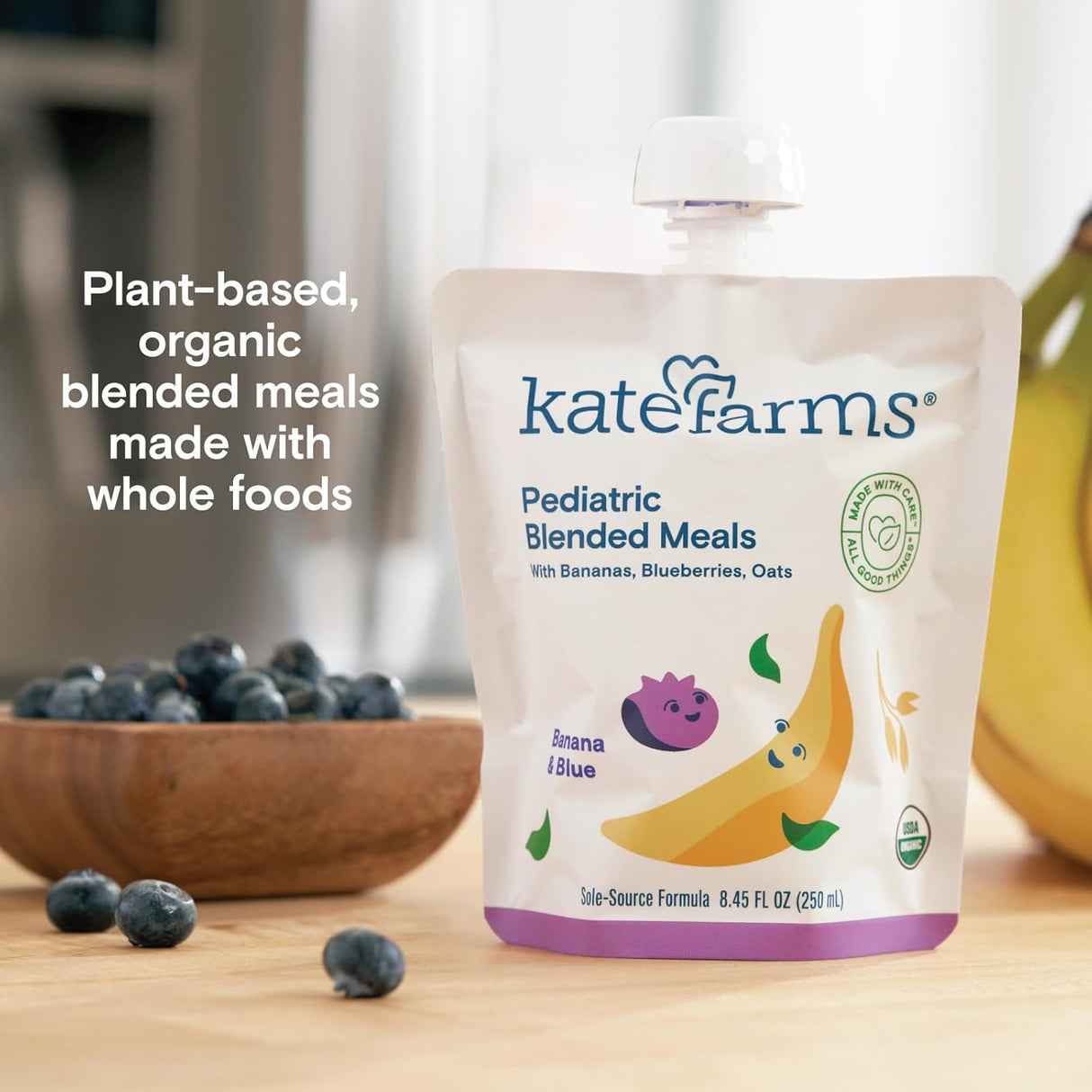A pouch of Kate Farms Pediatric Blended Meals, Banana & Blueberry, CS/12 sits by fresh fruit. Text beside it reads: Plant-based, organic nutrition with whole foods—ideal as a pediatric blended meal or tube feeding formula.