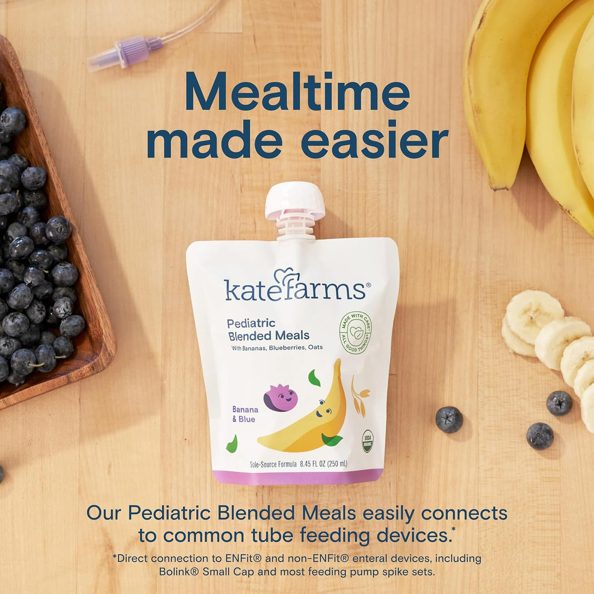 A pouch of Kate Farms Pediatric Blended Meals, Banana & Blueberry, CS/12 sits on a wooden table with blueberries, banana slices, a whole banana, and a feeding tube connector. Text: Organic nutrition for easier mealtime from Kate Farms.
