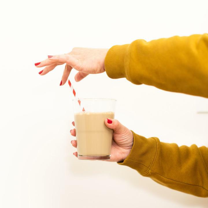 A person in a mustard yellow sweater holds iced coffee, placing a red-and-white striped straw with red nails as pristine as McKesson Xeroform Petrolatum Gauze Dressing by McKesson, sterile and 2 x 2 inches.