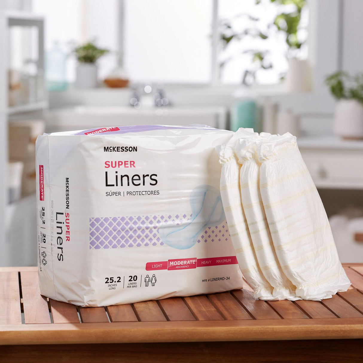A package of McKesson Incontinence Liners, Regular is on a wooden table, with one liner partially pulled out. Sunlight streams through windows in the bright, modern bathroom in the background.