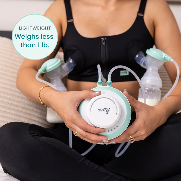 A person wearing a black bra uses the Motif Twist Double Electric Breast Pump by Motif, holding its lightweight main unit (weighs less than 1 lb), with two attached bottles partially filled with milk.