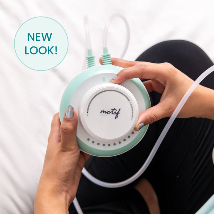 A person holds a mint green and white Motif Twist Double Electric Breast Pump with hospital-strength suction, tubes attached, sitting cross-legged on a black surface. A teal circle on the left reads NEW LOOK!.