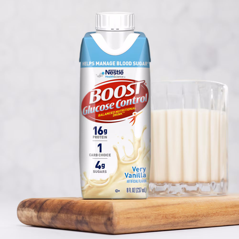 A carton of Nestle Nutrition Glucose Control Nutritional Drink, Very Vanilla (CS/24) sits on a wooden board beside a glass of vanilla drink, providing a low glycemic option for diabetes meal replacement against a softly blurred background.