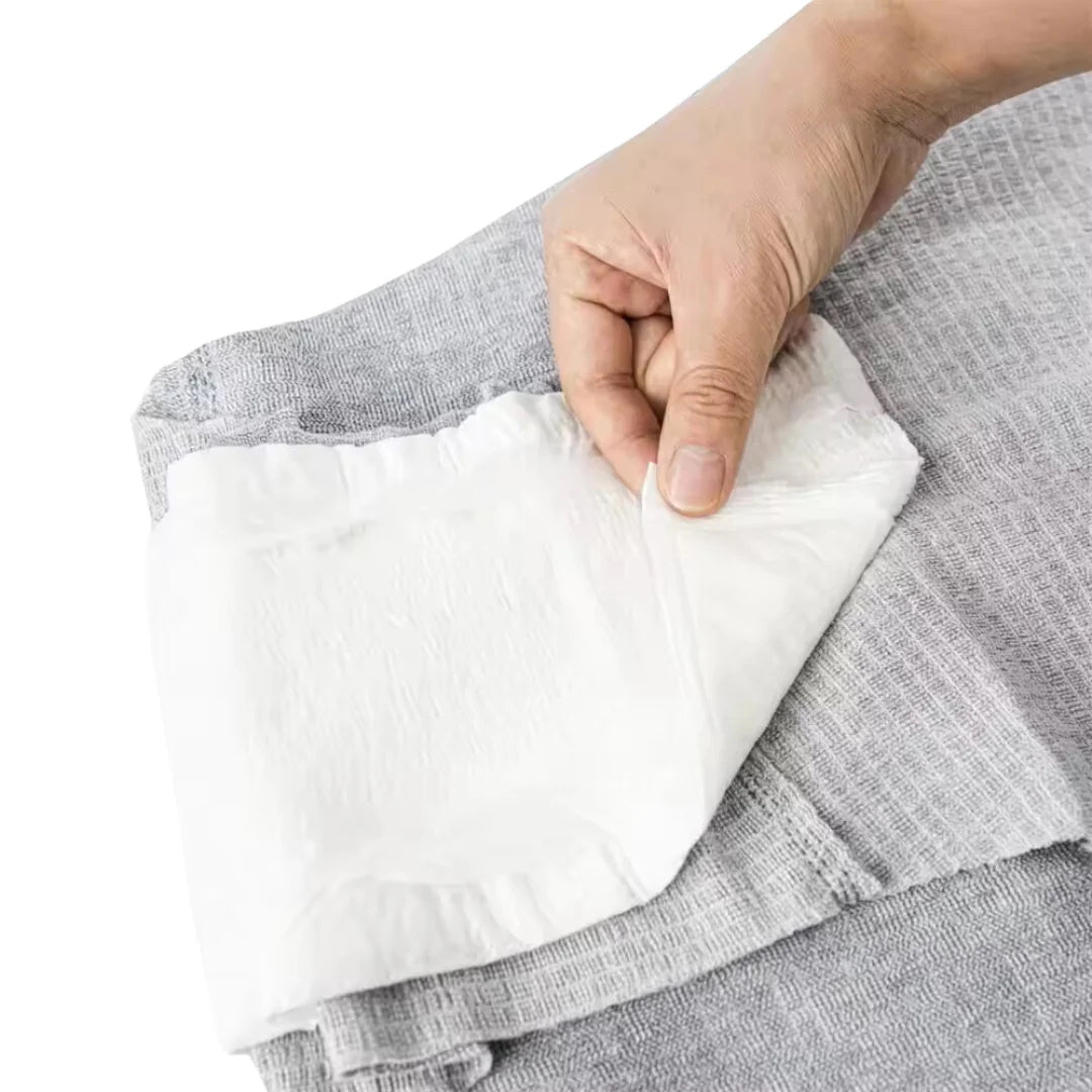 A hand lifts a Nexwear Mens Incontinence Underwear from a stack of gray textured fabric, with the product displayed against a plain background.