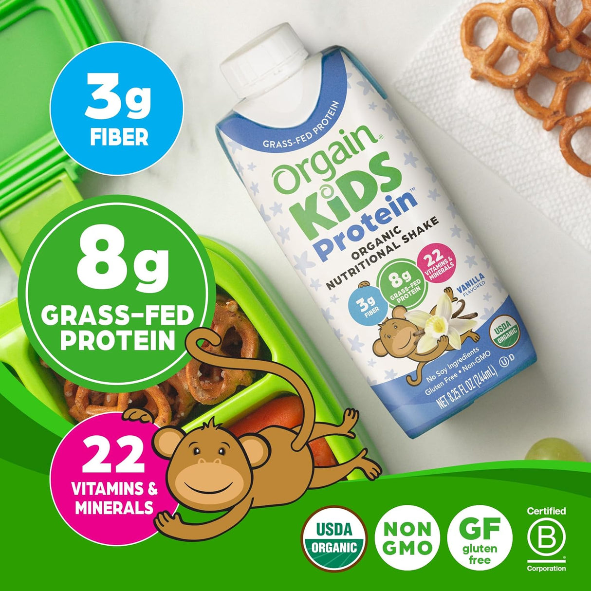 A carton of Orgain Organic Kids Nutritional Grass-Fed Protein Shake, Vanilla, Pack of 12 sits by a green lunchbox with pretzels. Text highlights 3g fiber, 8g grass-fed protein, 22 vitamins & minerals, certifications, and a cartoon monkey.