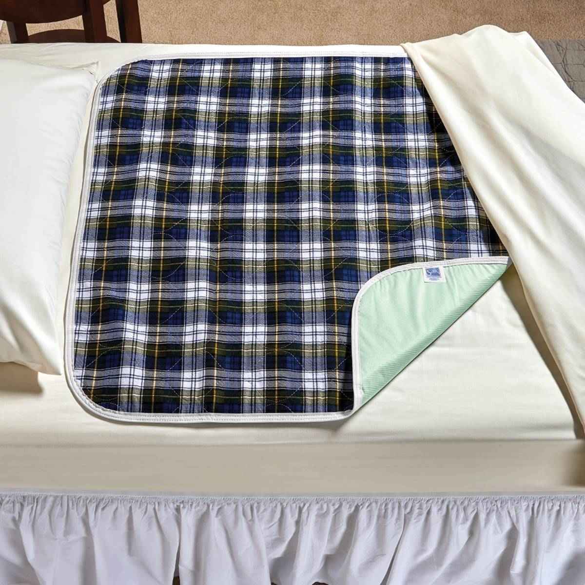 The Salk CareFor Deluxe Plaid Underpad by Salk features a blue, black, and white checked waterproof design with a light green underside—ideal reusable protection for urinary incontinence. Shown on white bed sheets, its partially folded at one corner.