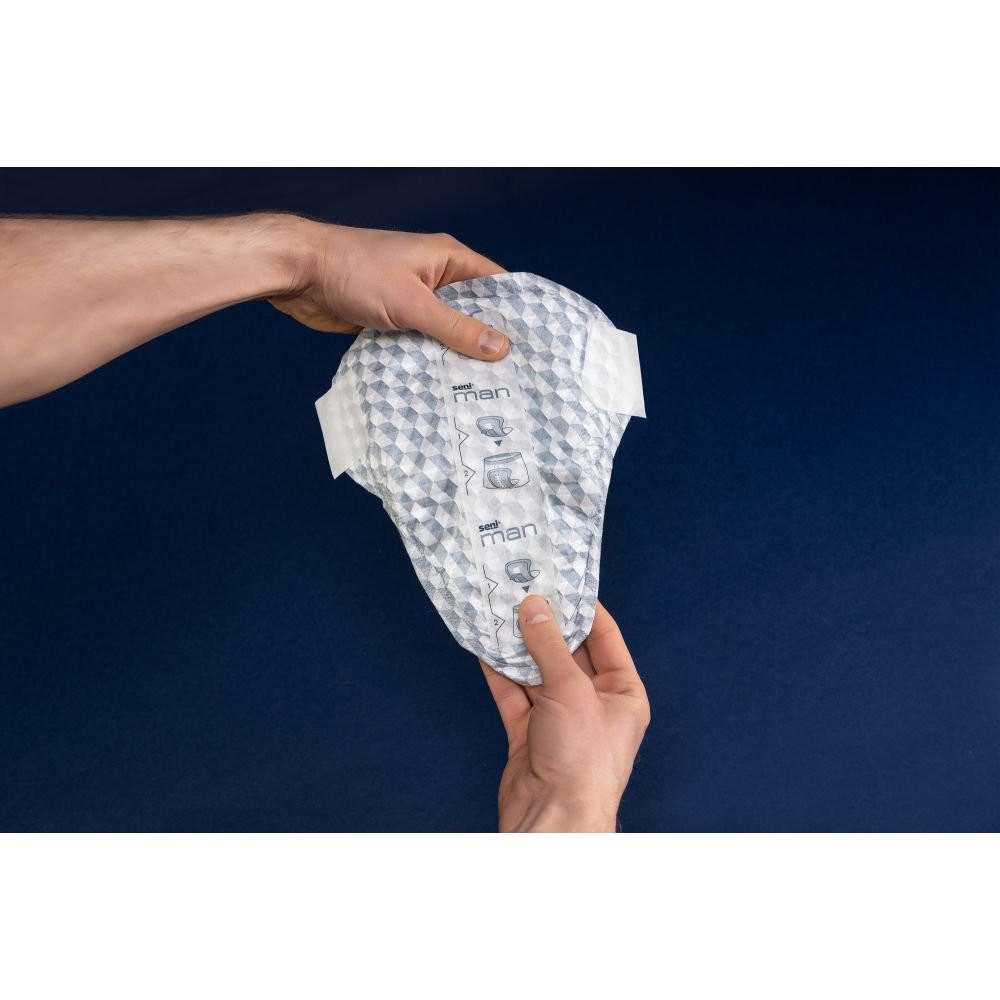 A person holds a white Seni Man Active Guard by Seni, a light absorbency incontinence product for men with a textured surface and tab extensions, against a dark blue background.