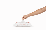 A hand pulls a Tranquility Cleansing Wipe with Aloe from the mostly white package with orange accents, set against a white background, emphasizing the gentle care these wipes provide for delicate skin.