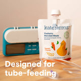 A pouch of Kate Farms Pediatric Blended Meals, Squash & Carrot, CS/12 by Kate Farms is displayed before a blue medical device. White text says "Designed for plant-based tube feeding," with a clear feeding tube in the foreground.