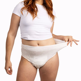 A woman in a white crop top shows the stretch and comfort of NorthShore GoSupreme Lite Pull-On Underwear by pulling the waistband outward, highlighting their reliable leak protection and easy-to-wear design.