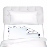 A white bed with a tufted headboard, white pillow, and blanket partially pulled back reveals NorthShore MagicSorb Air Super-Absorbent Disposable Underpads beneath for maximum absorbency.